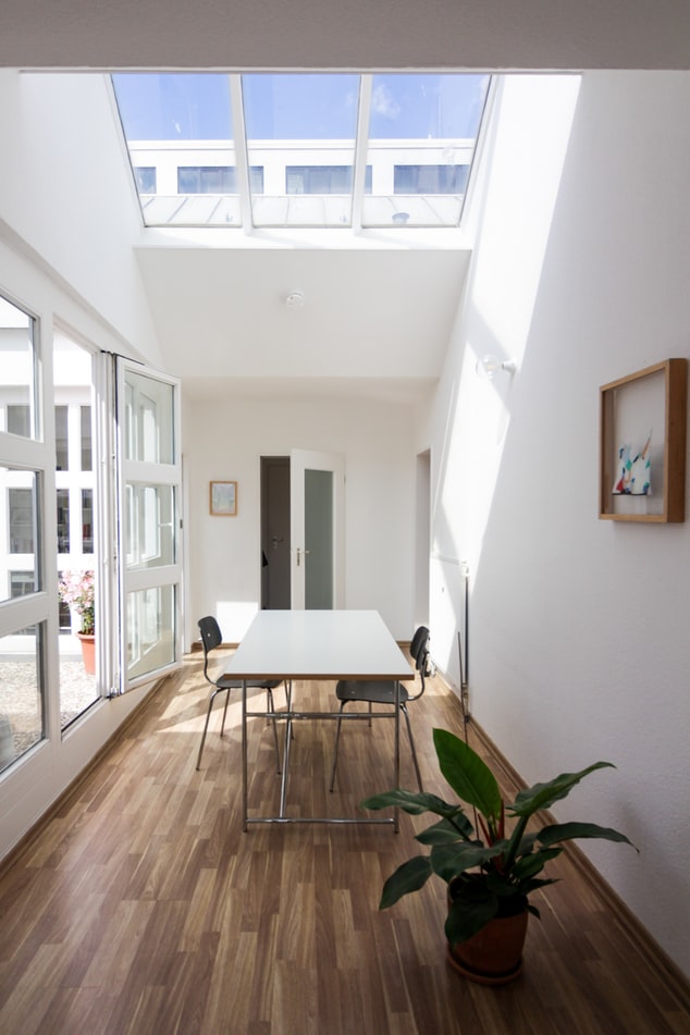 telhas-translucidas-casa.com-4-unsplash-beazy Sala com uma mesa e duas cadeiras, com piso de madeira, porta de correr de vidro e clarabóia no teto