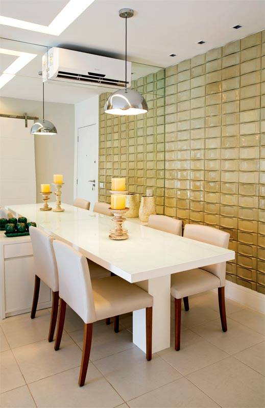 Sobre a mesa de jantar, a luz direta vem de um pendente. Dicroicas destacam a parede coberta de revestimento ciment&iacute;cio, que d&aacute; volume &agrave; superf&iacute;cie, dispensando ornamentos. Projeto das arquitetas Elise e Evelyn Drummond. Mesa de laminado e cadeiras revestidas de linho.