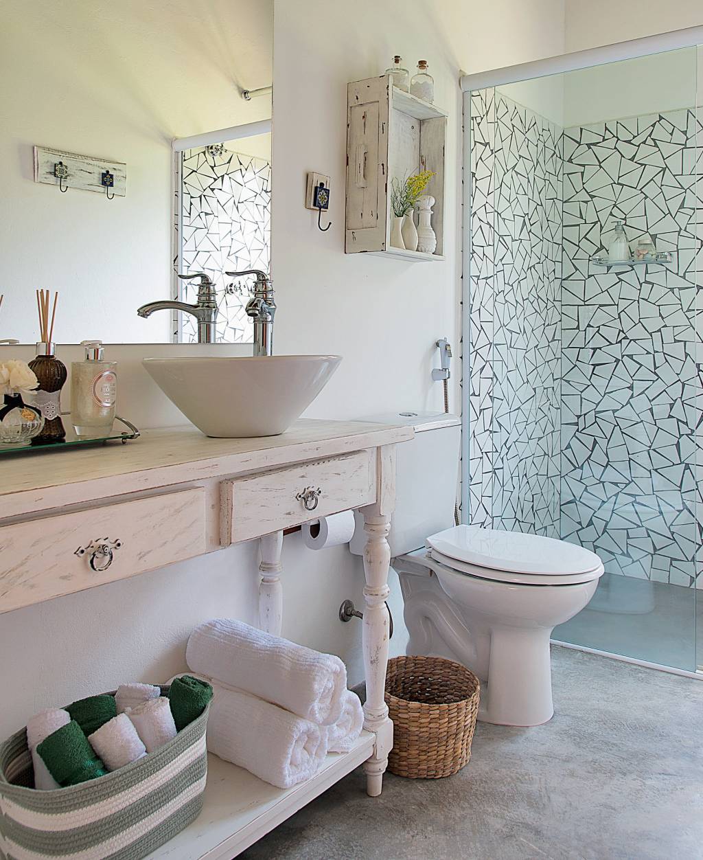 Um estilo de decora&ccedil;&atilde;o mais afetiva se revela neste banheiro de uma casa de campo em Ibi&uacute;na, SP. Assinado pela arquiteta Beatriz Castanho, o projeto exibe elementos r&uacute;sticos, como o aparador e a prateleira com pintura desgastada, o piso de cimento queimado e os caquinhos de azulejo (Arhus Alto Brilho Branco, de 32 x 57 cm, da Cecafi. C&C, R$ 11,90 o m&sup2;).
