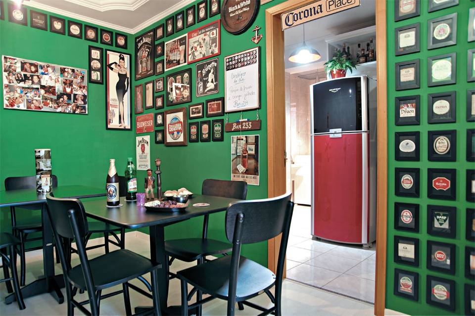 No lugar do sof&aacute;, duas mesinhas de madeira laqueadas, seis cadeiras na cor tabaco e duas banquetas altas (para o balc&atilde;o) mob&iacute;liam o espa&ccedil;o com lugares para as visitas se acomodarem nesta sala de jantar que imita um pub irland&ecirc;s e exibe porta-copos, r&oacute;tulos emoldurados.