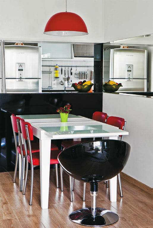 Um espelho cobre toda a largura da parede no canto de refei&ccedil;&otilde;es. A altura tamb&eacute;m tem sua raz&atilde;o: &eacute; id&ecirc;ntica &agrave; do v&atilde;o entre a cozinha e a sala. Na face vista da sala, o balc&atilde;o &eacute; revestido de um elegante laminado preto brilhante. Se desencostada da parede, a mesa recebe at&eacute; 8 pessoas.