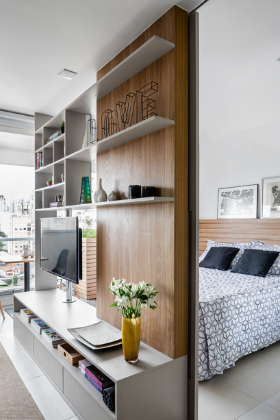 A estante com prateleiras vazadas não pesa no visual e ainda comunica os ambientes. O suporte da TV gira a fim de que ela se volte tanto para o quarto como para a sala. A estante com prateleiras vazadas não pesa no visual e ainda comunica os ambientes. O suporte da TV gira a fim de que ela se volte tanto para o quarto como para a sala.