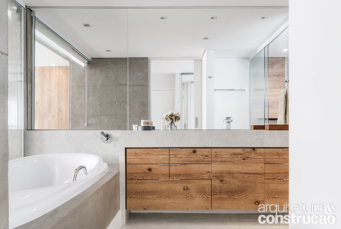 Conquistar um ambiente com ares de spa, que inclu&iacute;sse uma banheira (Elegance, da Pretty Jet): para atender ao desejo da moradora, o c&ocirc;modo foi atualizado pelo escrit&oacute;rio D&eacute;cio Navarro Arquitetura de Ideias. Da nova entrada, agora se v&ecirc; a bancada com cuba esculpida de porcelanato Broadway Lime (60 x 120 cm, da Portobello), com execu&ccedil;&atilde;o da Latina Cer&acirc;mica. O revestimento se repete no piso e dialoga com a coluna, coberta de massa especial para criar o efeito de concreto (obra do pintor Varlei C&acirc;ndido). A marcenaria de laminado imitando madeira de demoli&ccedil;&atilde;o (Marcenaria M&atilde;os de Ouro) esquenta o local. &ldquo;O uso de poucos materiais e a soma de elementos r&uacute;sticos e sofisticados d&atilde;o o tom atual ao ambiente&rdquo;, diz o arquiteto D&eacute;cio.