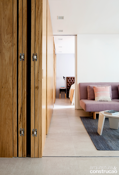 Da sala, o olhar alcan&ccedil;a a su&iacute;te, ao fundo. A parede da cabeceira &eacute; a &uacute;nica que ostenta alguma cor al&eacute;m do branco, um cinza leve (Suvinil, ref. Tit&acirc;nio). No piso, o porcelanato de 60 x 120 cm tem um tom parecido (Portobello, ref. Bras&iacute;lia). Tapete da By Kamy.