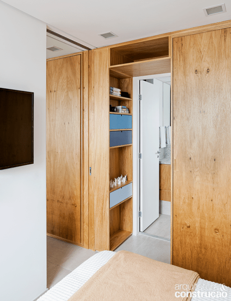 Todos os espa&ccedil;os ganhos com a marcenaria foram utilizados, caso da entrada do banheiro do casal. &ldquo;N&atilde;o havia ali profundidade para uma porta, ent&atilde;o aproveitamos o trecho com nichos e um maleiro em cima&rdquo;, detalha Aline.