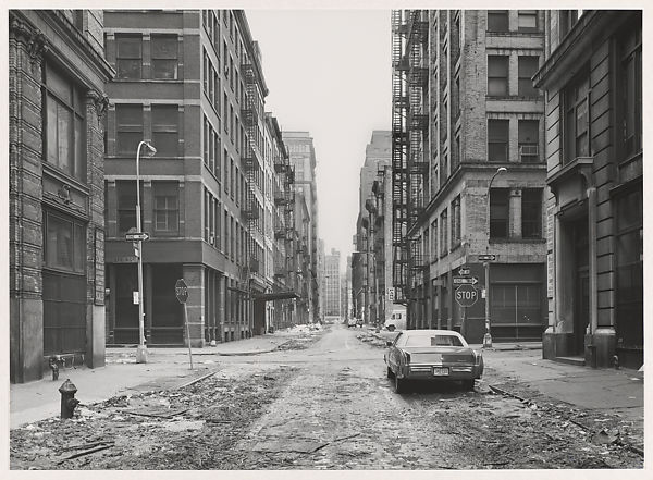 o-que-e-loft-Thomas-Struth-Crosby-Street-1978-Met-Museum fotografia preta e branca de rua vazia com apenas um carro e prédios velhos