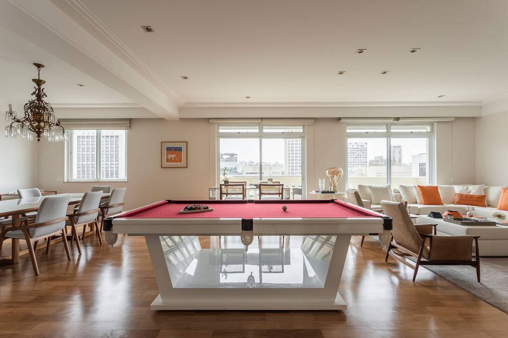 Sala de estar integrada, com piso de taco e mesa de sinuca com tecido vermelho no centro assinado por Gabriela Casagrande Arquitetura