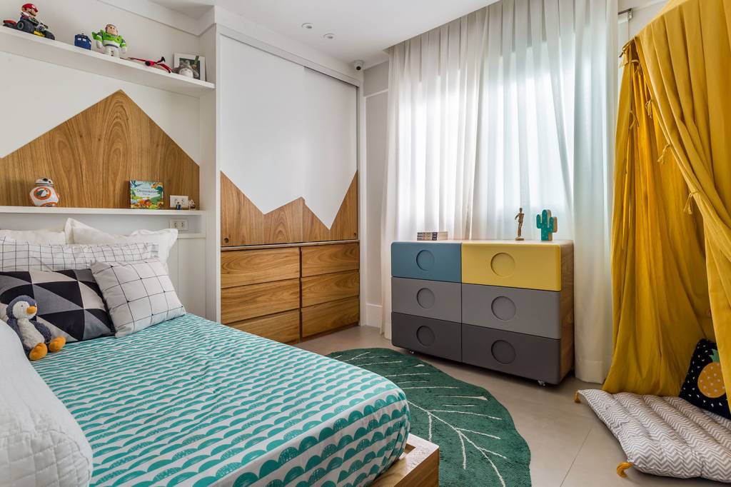 no-rio-cobertura-duplex-de-130-m²-ganha-projeto-de-decoracao-e-marcenaria-casa.com-co+lab-arq-e-int-luiza-schreier-15 Quarto infantil, com roupa de cama verde, tapete em fomarto de planta, guarda roupa com desenho de montanha, e cômoda nas cores cinza escuro, cinza claro, azul e amarelo