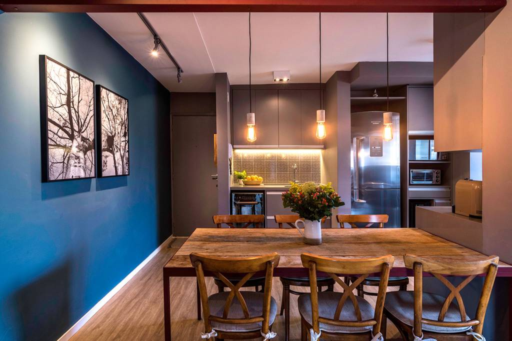 reforma-garante-personalidade-e-conforto-para-um-apartamento-de-70-m²-casa.com-hoearquitetura-eli-k-hayasaka-6-sala-de-jantar Sala de estar jantar, com piso de madeira, e cozinha com móveis marrons e aprede azul à esquerda
