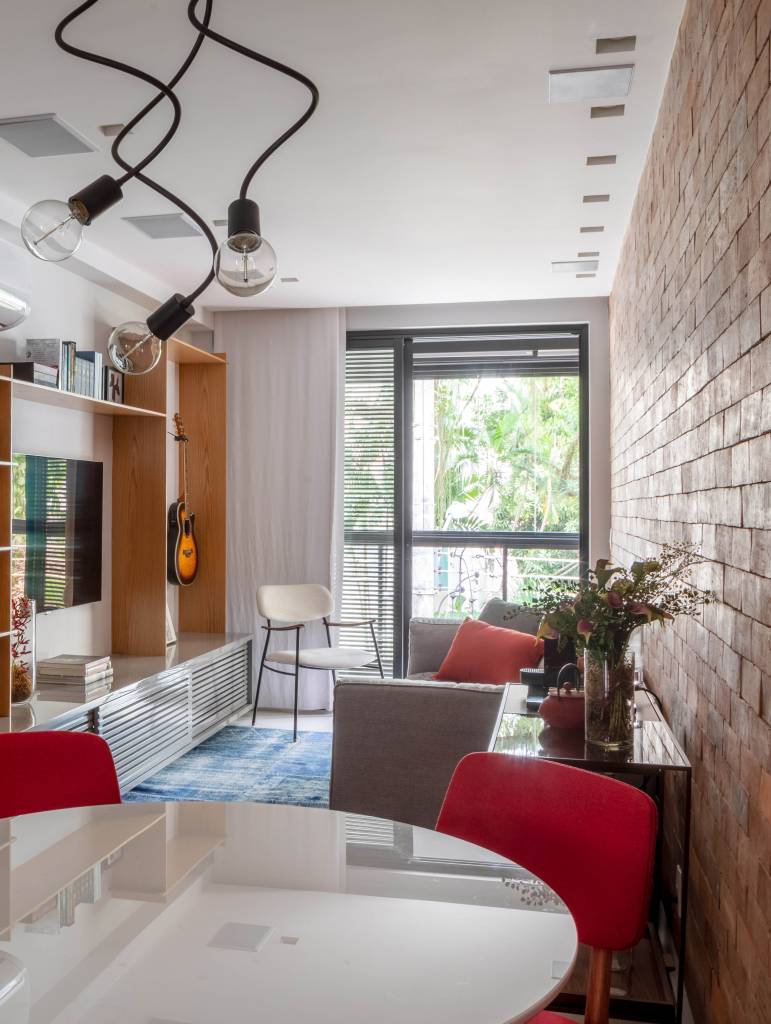 4-apê-de-65-m-2-recebe-estilo-contemporâneo-urbano-e-tons-neutros Sala de estar integrada ao jantar e à varanda com parede de tijolinhos e cadeiras vermelhas