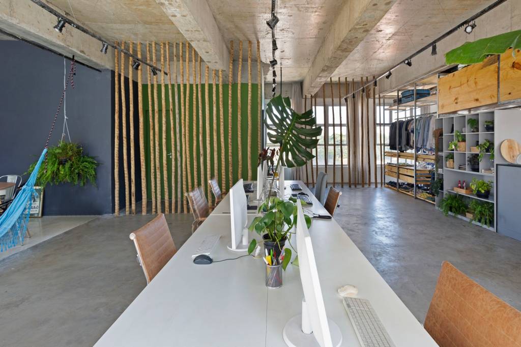 arquiteto-transforma-sala-comercial-em-loft-julia-ribeiro-escritorio-divisorias-com-marcenaria Escritório com bancada grande para vários computadores, com plantas e divisória de caibro roliço ao fundo