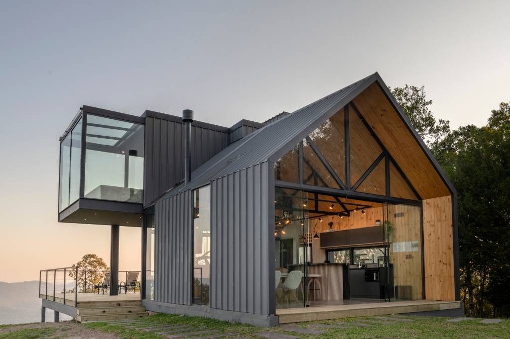 Cabana metálica com interior revestido em madeira, com vista para paisagem de montanha