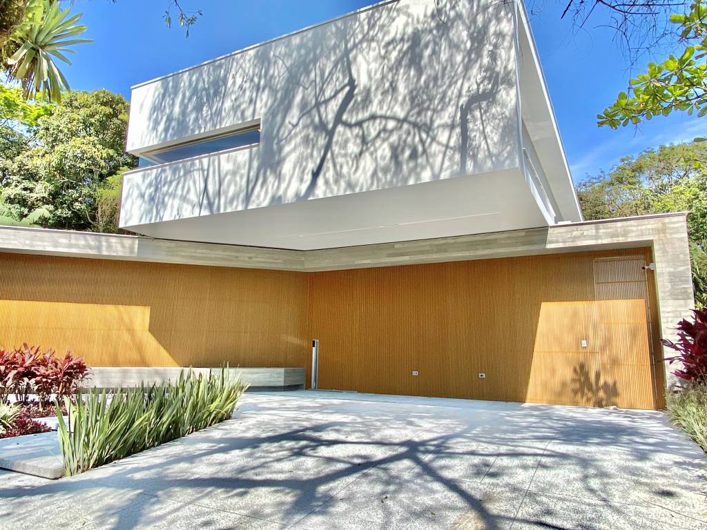 entrada frontal de casa com garagem que recebe um volume de concreto em balanço que cria a área coberta para quem entra e protege os carros.