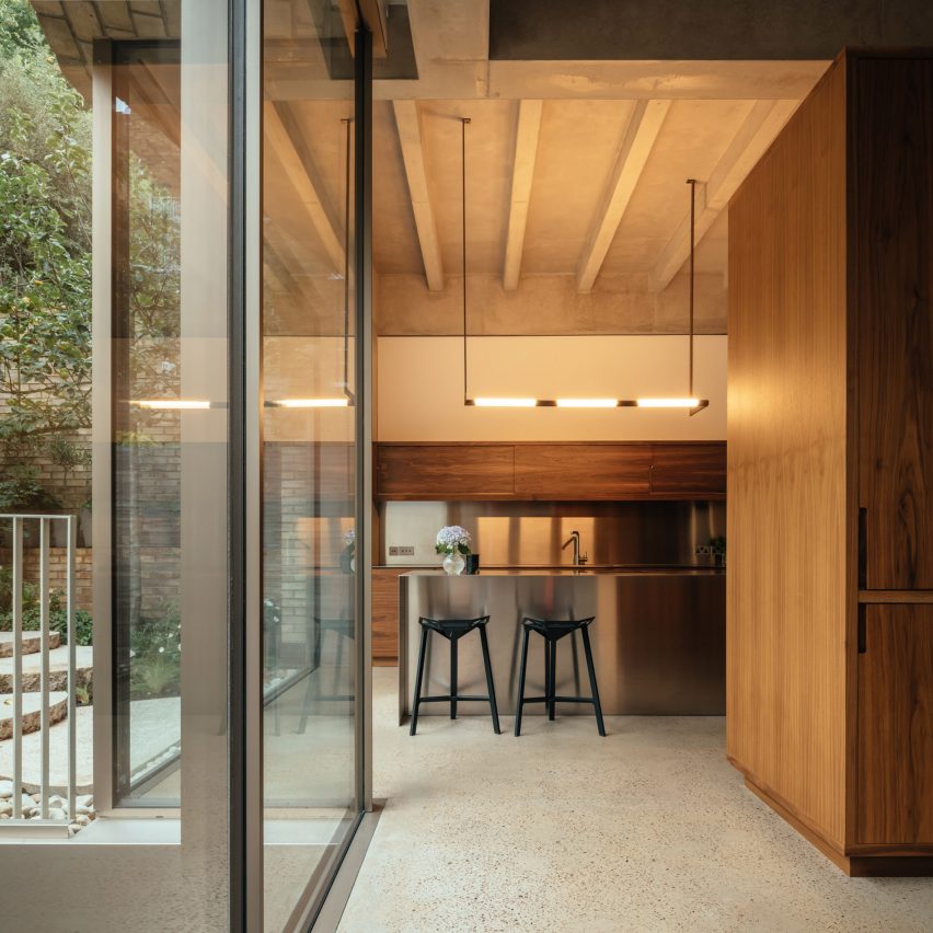 casa-vitoriana-londres-ganha-dois-andares-subsolo-jim-stephenson-sala-de-jantar-armario-madeira-caixilhos-vidro Porta de vidro grande dá acesso a sala de jantar com armário de madeira grande, bancada em inox com duas banquetas e iluminação com pendente moderno.