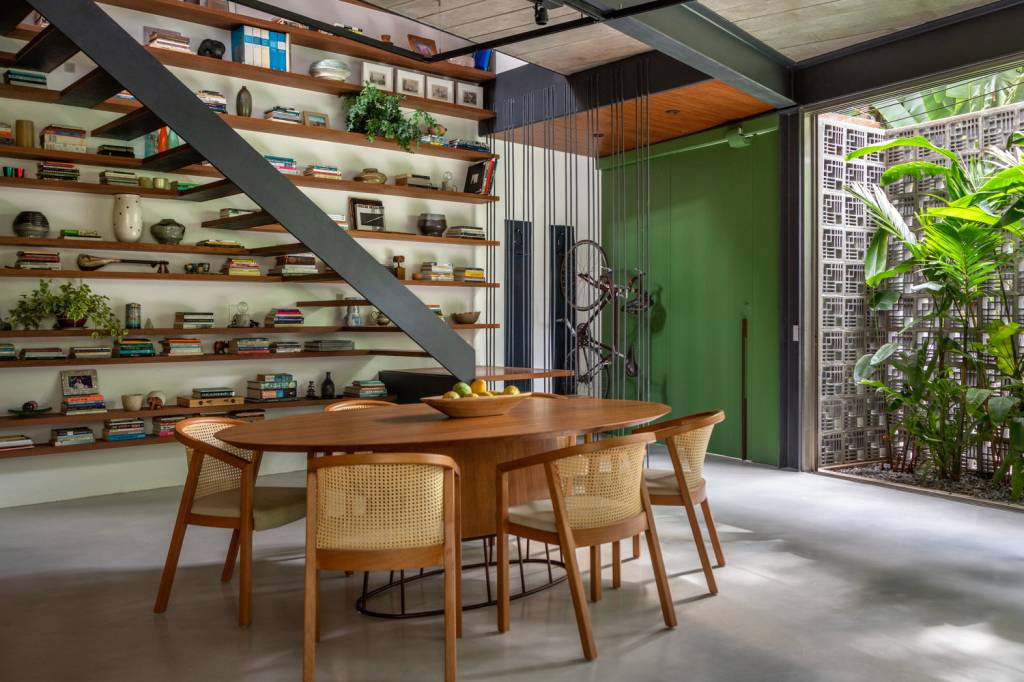 cobogo-madeira-certificada-fachada-iluminada-com-jardim-andre-nazareth-jardim-interno-estante-escada Sala de jantar e estar tem jardim interno e estante de livros na parede com escada de alumínio