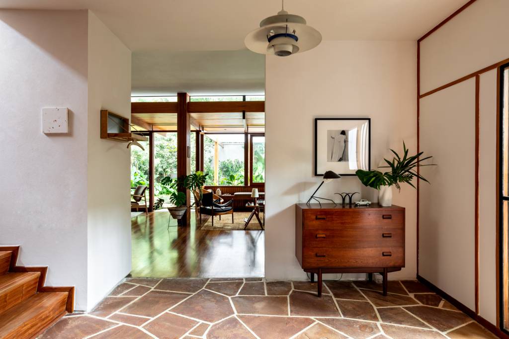 conheca-restauracao-casa-thompsons-hess-fran-parente-piso-pedra-mobiliario-moderno Imagem mostra piso de pedra em uma sala íntima, que foi recuperado na restauração, além de uma cômoda com objetos decorativos e sala de estar ao fundo.
