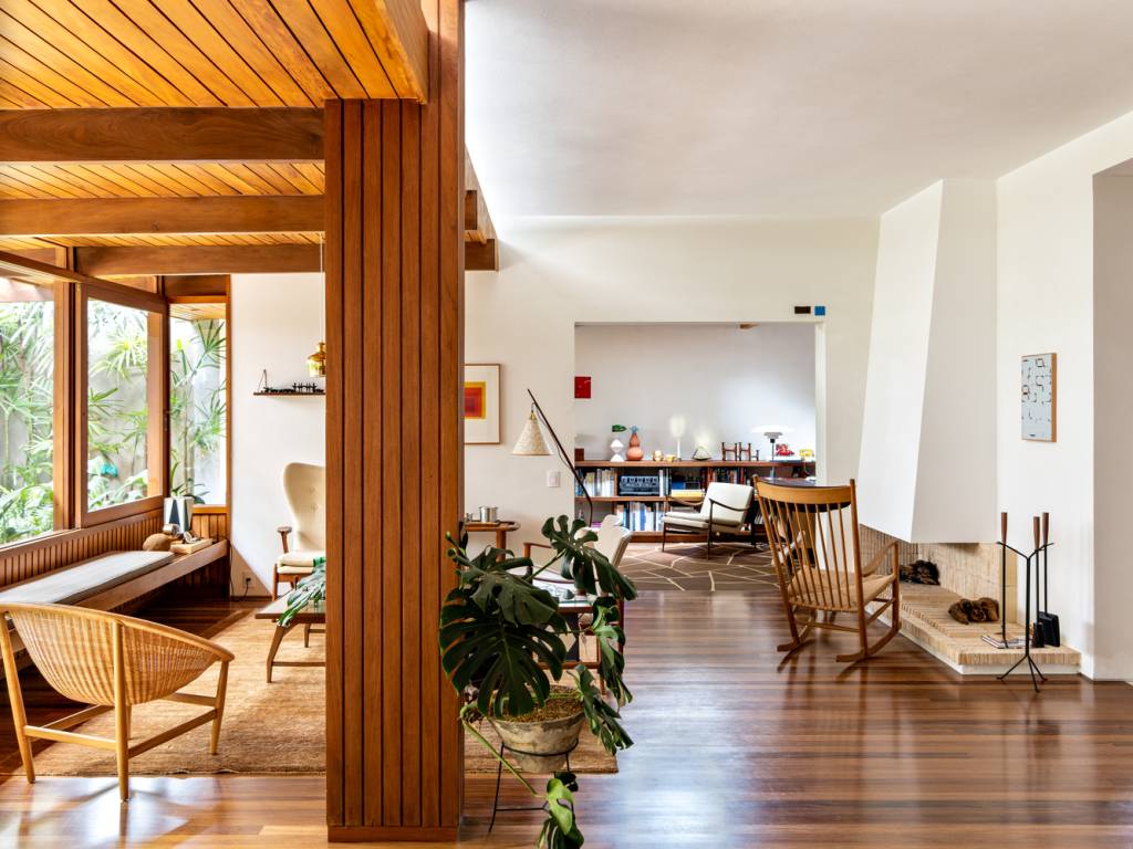 conheca-restauracao-casa-thompsons-hess-fran-parente-sala-de-estar-lareira-piso-madeira Sala de estar com piso de madeira corrida, mobiliário modernista, lareira embutida na parede e coluna revestida de madeira em primeiro plano.