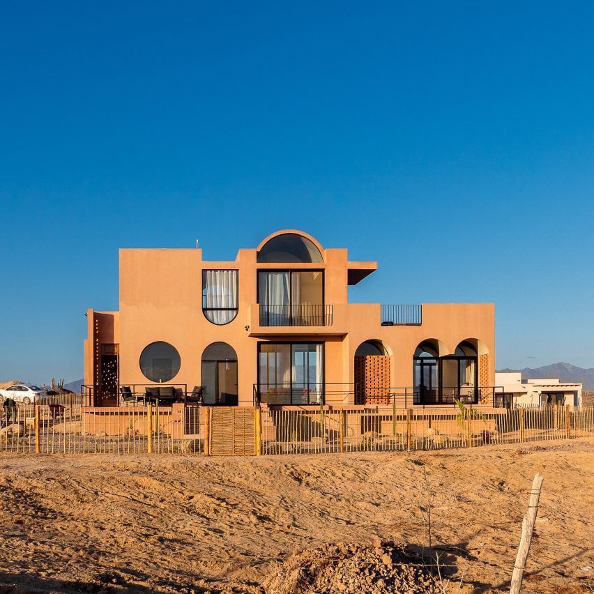 quem-disse-concreto-precisa-ser-cinza-miguel-angel-vazquez-calanchini-fachada-casa-concreto-avermelhado Paisagem desértica do México com casa que tem fachada em tom de terra natural, arcos, uma janela redonda e abóbada.