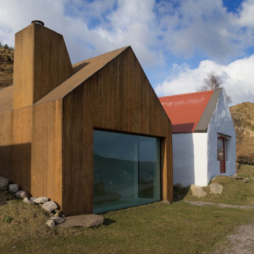 Casa com fachada que lembra um celeiro, com tom de aço corrugado, ao lado de outra casa pintada de branco com telhado vermelho.