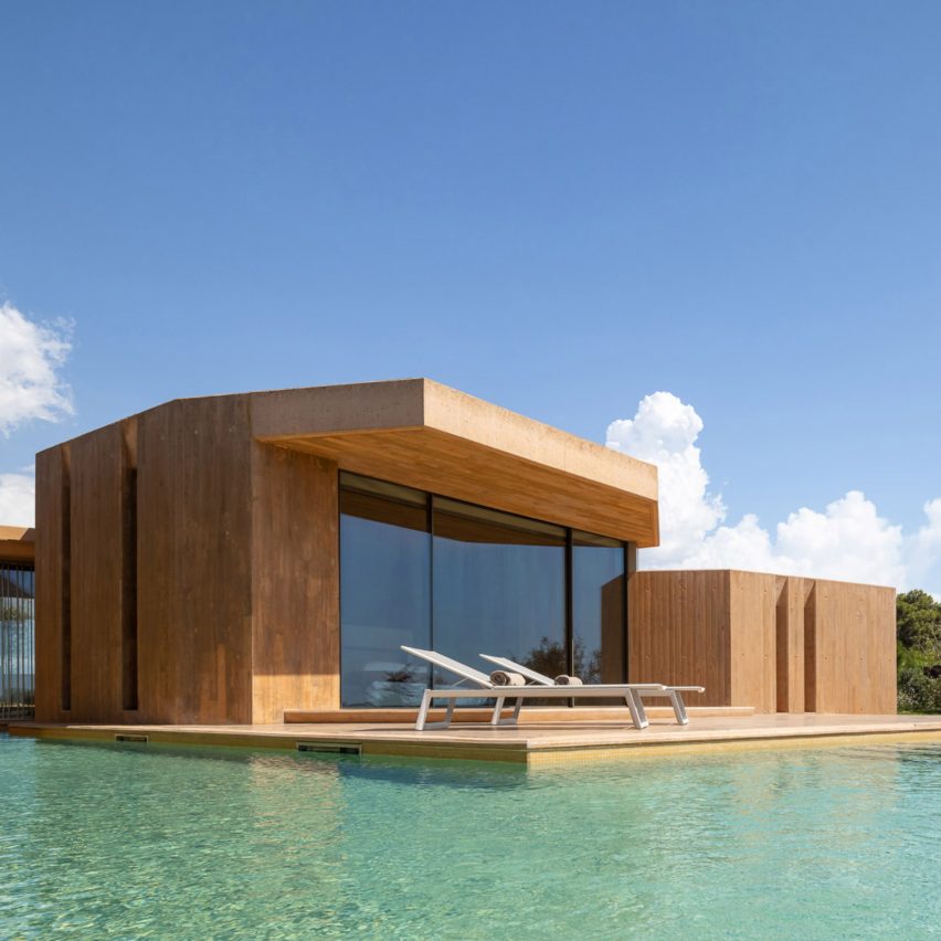 Casa de luxo com piscina tem fachada em tom de ferrugem e céu azul ao fundo.