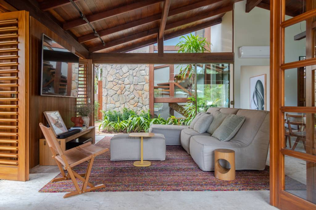 4-ar-de-cabana-e-praia-confira-o-projeto-desta-casa-de-250-m-2 Living com sofá cinza, tapete colorido e muita madeira