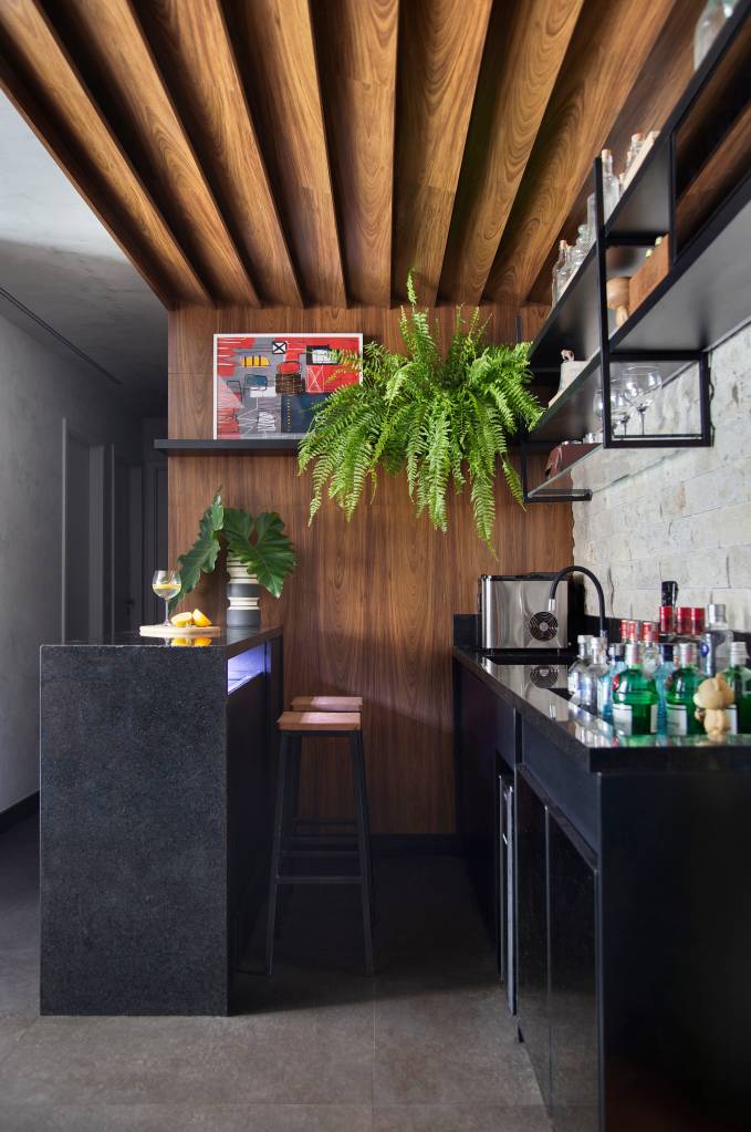 Apartamento masculino no bairro Santa Rosa em Niterói assinado pelo STUDIO LIVIA AMENDOLA _ foto 7-bar Home bar com bancada preta; samambaia suspensa; revestimento em madeira ripada