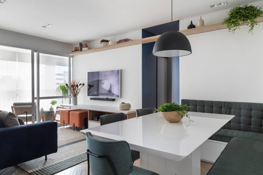 Confira-dicas-para-aqueles-que-pretendem-morar-sozinhos-Evelyn-Muller-ambientes-móveis-decoração-espaços-salas-integrados Salas de jantar e estar integradas. Na de jantar, há uma mesa branca sob uma luminária preta em forma de hemisfério. A sala de estar conta com um sofá, dois pufes e uma TV fixada na parede.