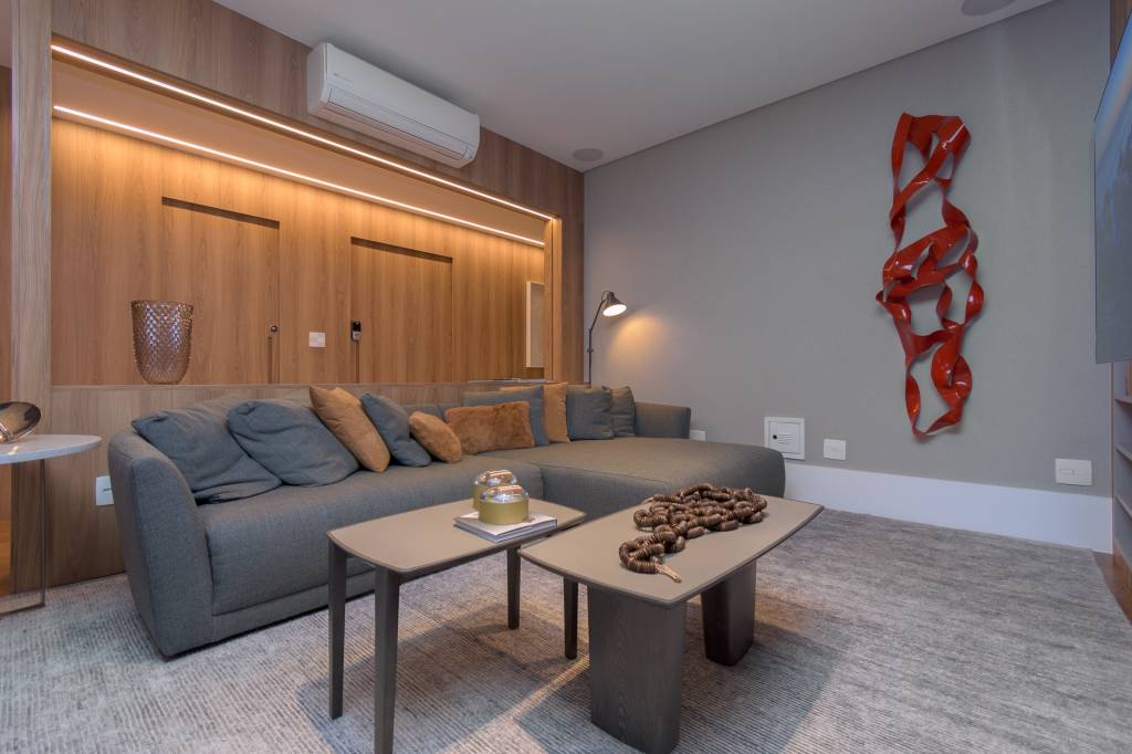 Dicas-para-valorizar-espaços-com-efeitos-incríveis-de-iluminação-Herman-Charles-Christ- Buzina-de-Imagem (5) Sala de estar com um grande sofá azul acinzentado. A parede atrás deste móvel é revestida de madeira e guarda fita de led que auxiliam na iluminação do ambiente.