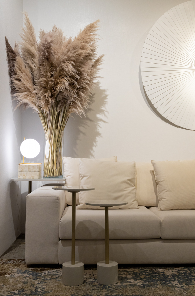Moderno-e-orgânico-a-trend-para-se-reconectar-com-a-natureza-Casa.com.br-Bia-Nauiack-decoração-dicas-inspiração Detalhe de sala de estar com sofá bege claro pequenas mesas de apoio de tampo redondo. No canto atrás do sofá um arranjo de folhas secas de cor próxima a do sofá.