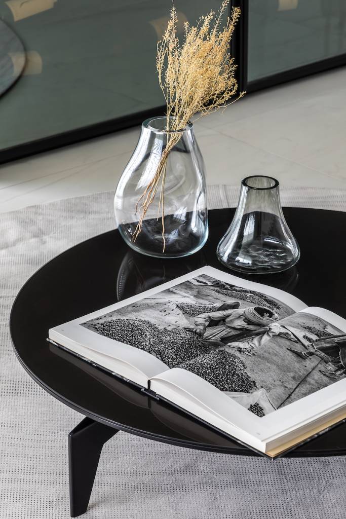 Moderno-e-orgânico-a-trend-para-se-reconectar-com-a-natureza-Casa.com.br-Eduardo-Macarios-decoração-dicas-inspiração Detalhe de mesa de centro preta, decorada por vasos de vidro em formas sinuosas. Um livro de fotografia aberto compõe a decoração.