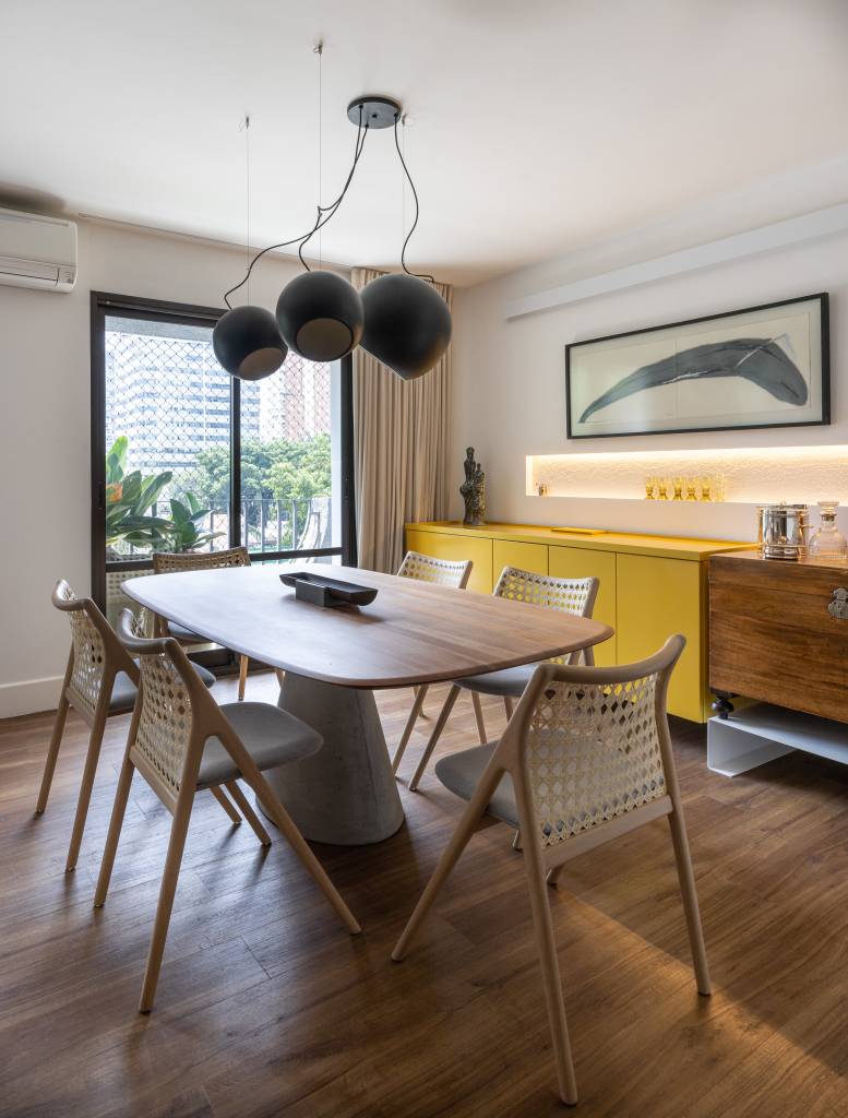 Sala de jantar com pendente; mesa em madeira com quatro lugares; aparador amarelo; nicho iluminado