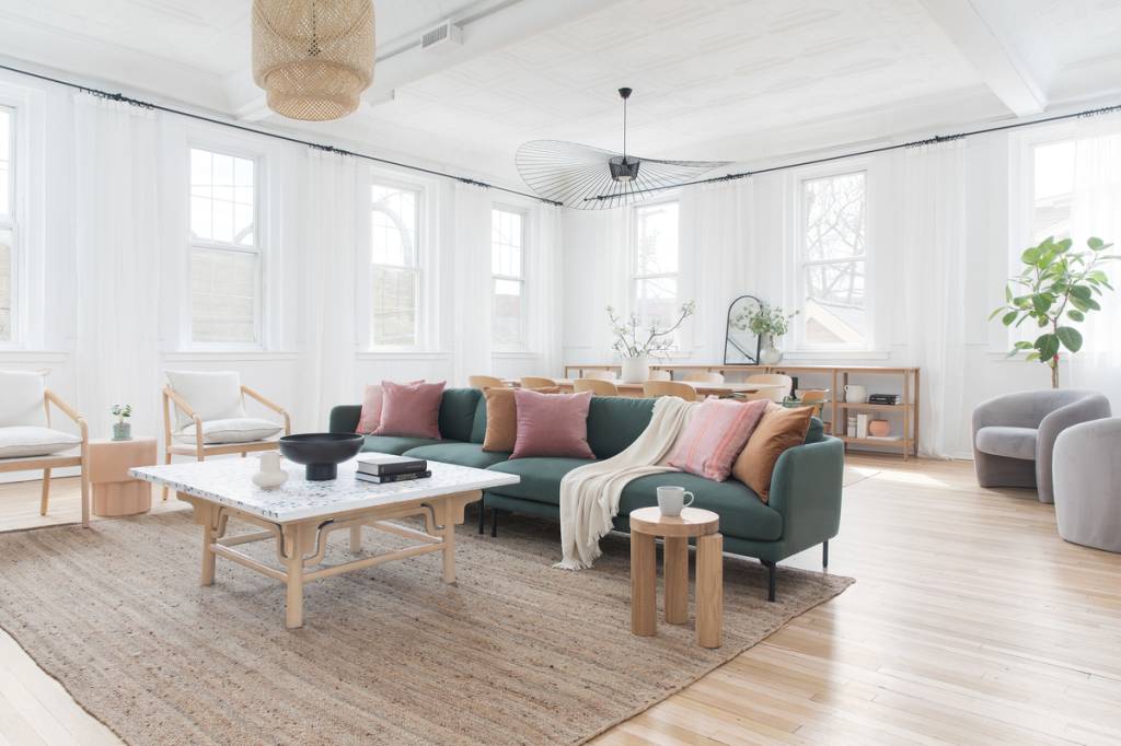 Sala com estilo clean e escandinavo; Sofá verde com almofadas rosa; mesa de centro em madeira; paredes brancas com muitas janelas