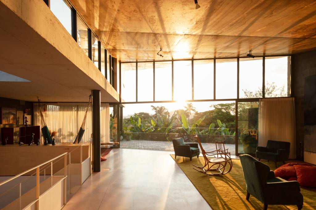 casa-sp-área-social-piso-superior-joão-morgado-sala-estar-entardecer-pe-direito-duplo Sala de estar ampla com painéis de vidro recebe luz do sol ao entardecer.