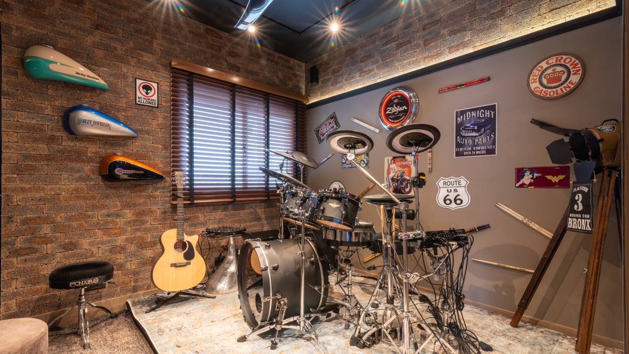 Sala de música com tapete, bateria, violão, paredes revestidas e visual de rock.