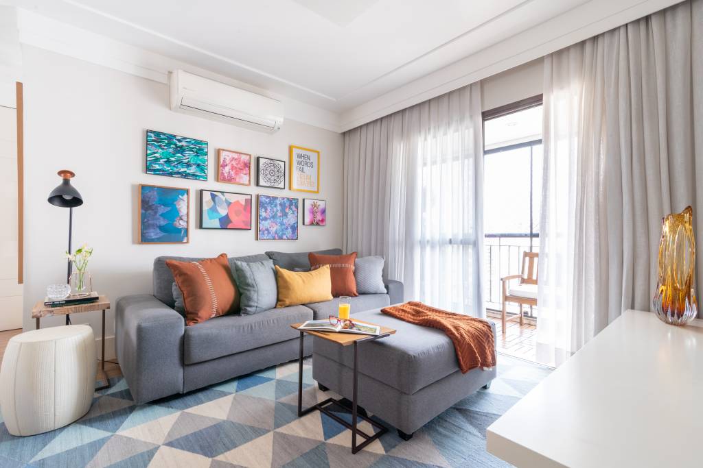 conforto-acustico-em-casa-julia-herman-sala-de-estar-sofa-cinza-quadros-coloridos-cortina-tapete-geometrico Sala de estar com varanda tem sofá cinza com almofadas coloridas, arranjo de quadros na parede, tapete grande geométrico e cortina.