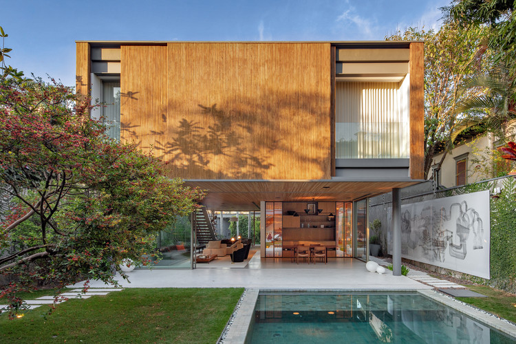 Fachada de casa com piso térreo com área social integrada ao paisagismo e à piscina, e piso superior com fechamento em ripado de pinus e aberturas de vidro.