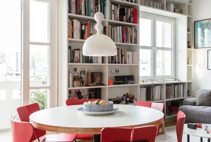 Sala de jantar com mesa redonda branca; estante com livros ao fundo; luminária