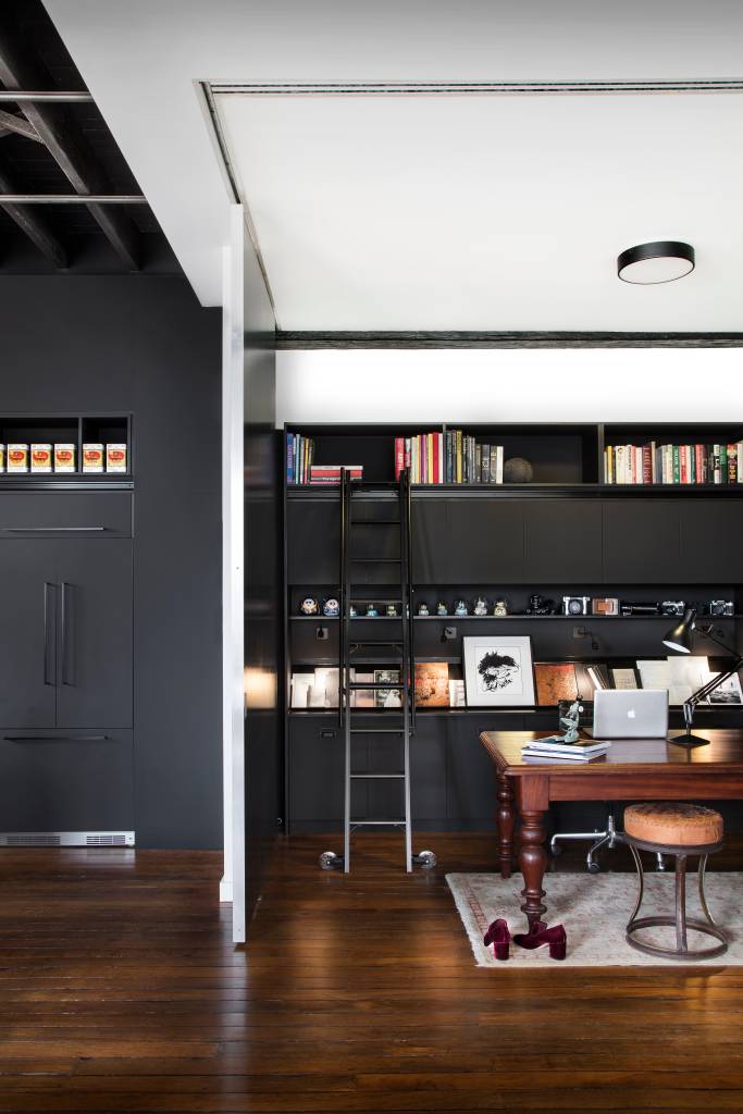 18-armazem-de-145-m-2-ganha-estilo-industrial-e-vira-casa-e-estudio-de-artista Sala de estar com estante preta, mesa de madeira e piso de carvalho