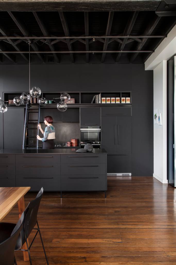 4-armazem-de-145-m-2-ganha-estilo-industrial-e-vira-casa-e-estudio-de-artista Sala de estar com estante preta e piso de madeira