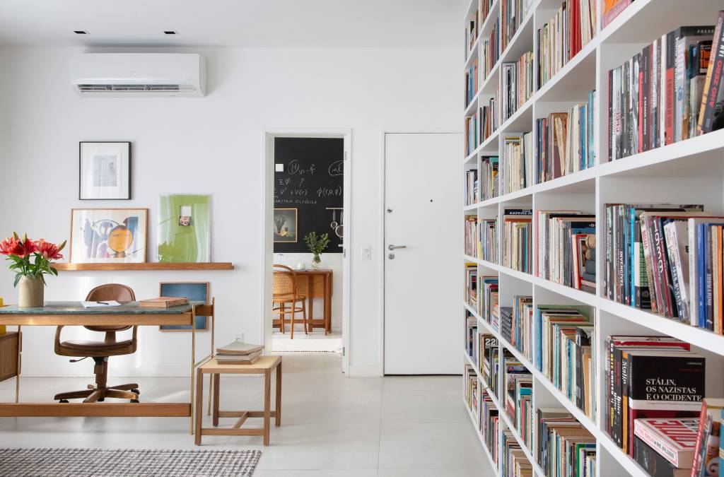 4-estante-com-mais-de-1500-livros-e-destaque-deste-ape-de-60-m-2-no-rio Sala de estar com décor claro, base branca e estante com muitos livros
