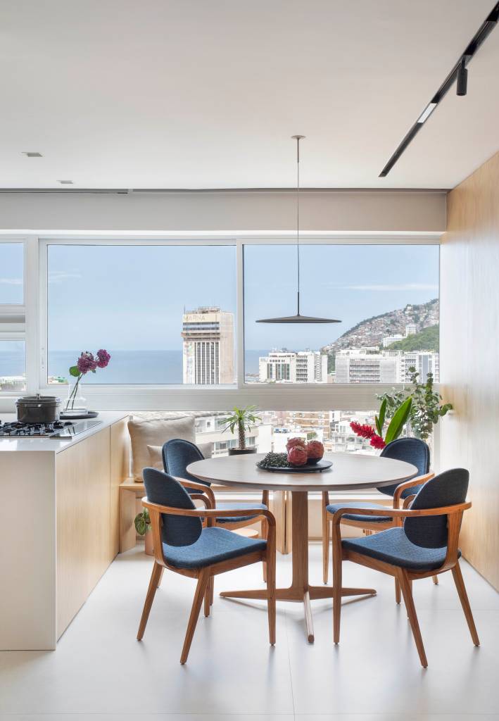 Sala de jantar com vista para o Rio de Janeiro com poltronas azuis e painel de madeira ao lado