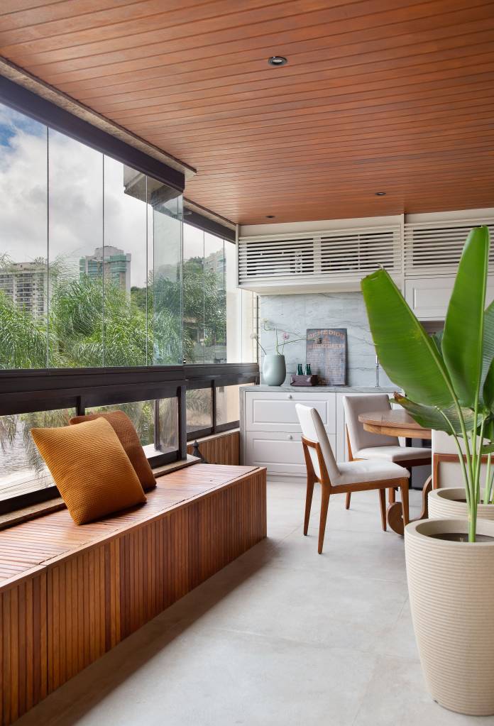8-base-neutra-design-assinado-e-vista-para-niteroi-veja-este-ape-de-290-m-2 Varanda com banco de madeira, cadeiras brancas e vaso com planta