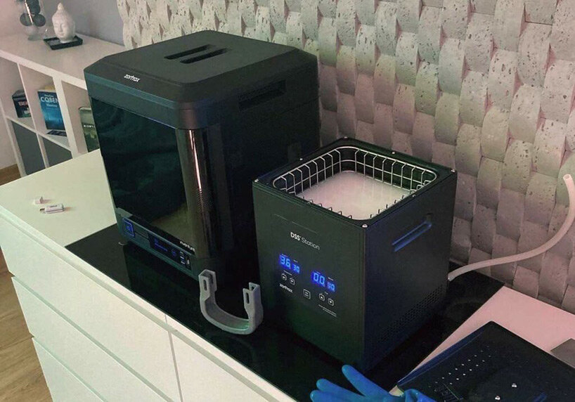 Impressora 3D e máquina para fazer molde sobre uma bancada. Os equipamentos tem formato de cubos.