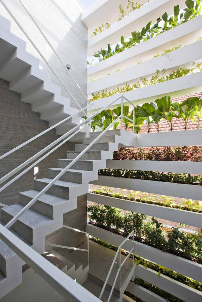 biofilia-fachada-verde-traz-benefícios-a-casa-vietna-hiroyuki-ori-escada-branca-jardim-vertical Foto mostra escada interna branca, com parede repleta de caixas de concreto que formam paredes verdes vazadas e cheias de vasos de plantas.