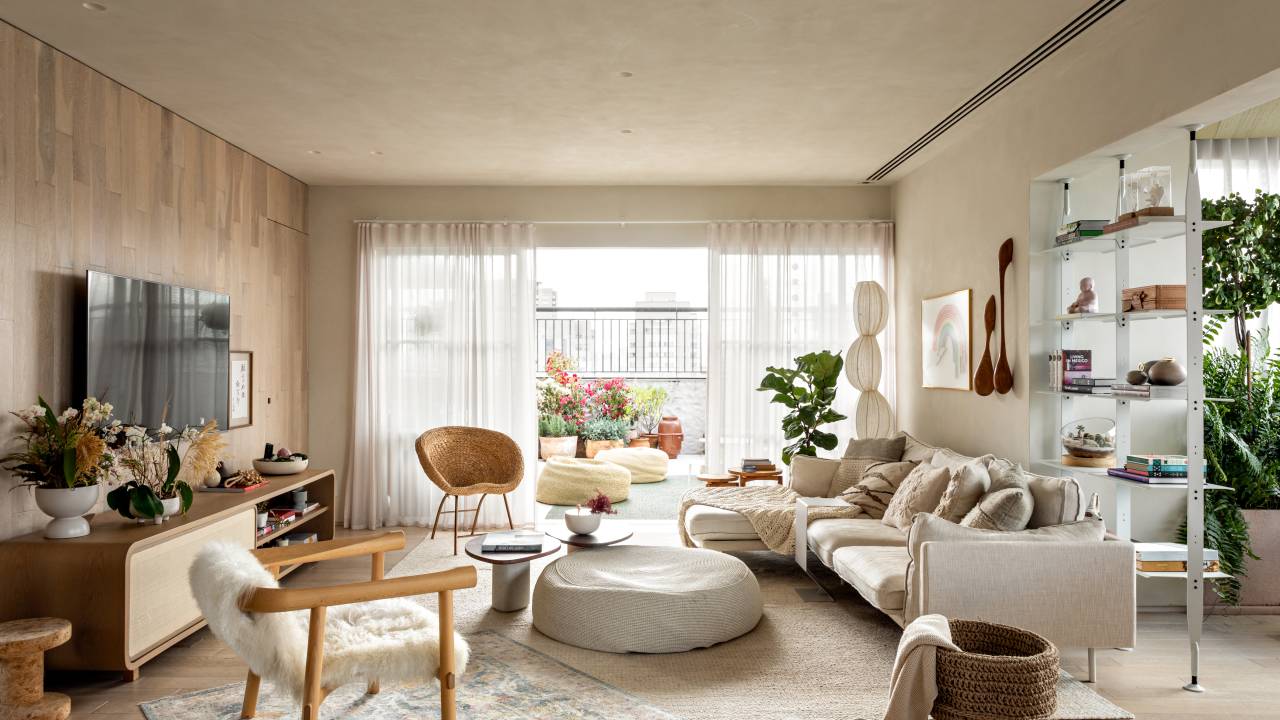 Sala com decoração neutra em tons terrosos; sofa branco, cadeiras, poltronas e pufe no centro