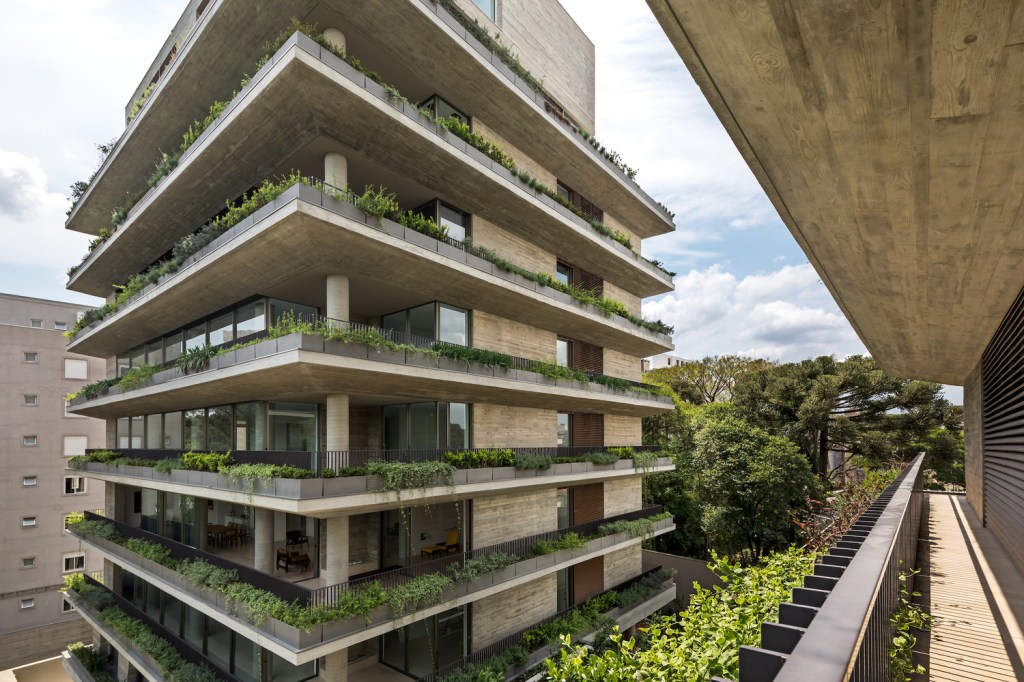 Foto mostra varandas de apartamentos com floreiras com vegetação abundante e jardins no condomínio.