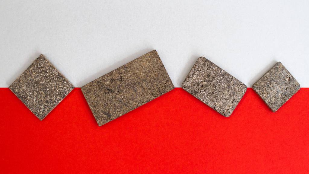 10-materiais-que-podem-mudar-a-construção-divulgação-dezeen-aglomerado-de-casca-de-batata Foto mostra dois pedaços de aglomerado em tons de marrom sobre fundo branco e vermelho.