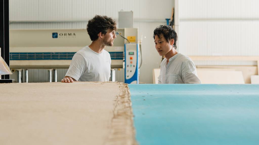 10-materiais-que-podem-mudar-a-construção-divulgação-dezeen-placa-de-papel-usado Foto mostra dois homens em frente a uma mesa onde se vê placas de papel.