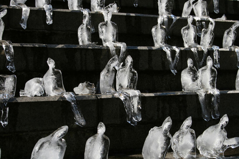 Essas esculturas de gelo alertam sobre mudanças climáticas-Designboom Néle Azevedo Fanca Cortez Pequenas esculturas de gelo derretendo de pessoas sentadas uma ao lado da outra de cabeças levemente baixas numa escadaria.