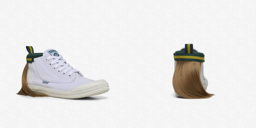 isso é um sapato com um mullet designboom volley (1) Tênis todo branco com uma mecha de cabelo presa na parte superior traseira, simulando um mullet. O cabelo é preso por uma tira de velcro que por fora é verde com uma listra amarela.